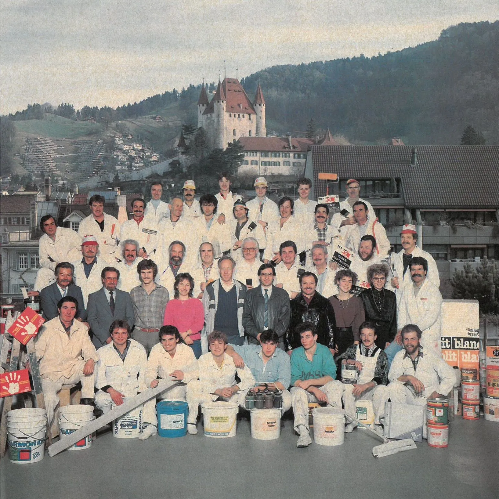 Gruppenbild der Kilchherr-Belegschaft 1988 mit Farbkübeln und Werkzeug, im Hintergrund Schloss Thun