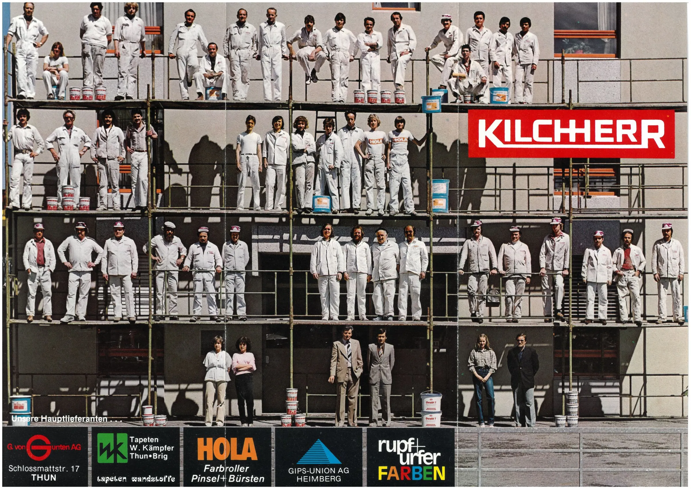 Das Kilchherr-Team in weissen Arbeitskleidern auf einem vierstöckigen Fassadengerüst, rechts das rote KILCHHERR-Banner