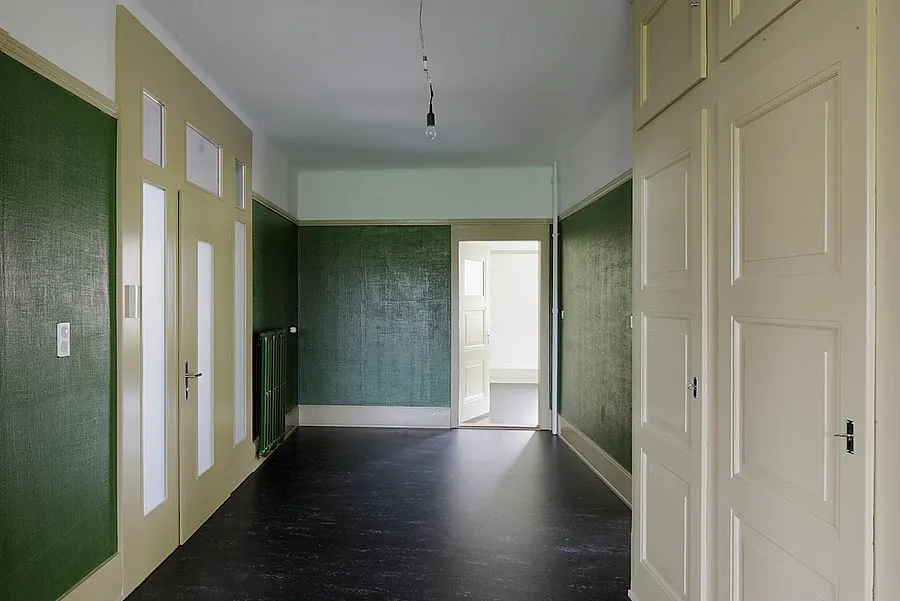Korridor einer Villa mit grünen Wänden, hellen Kassettentüren und dunklem Boden