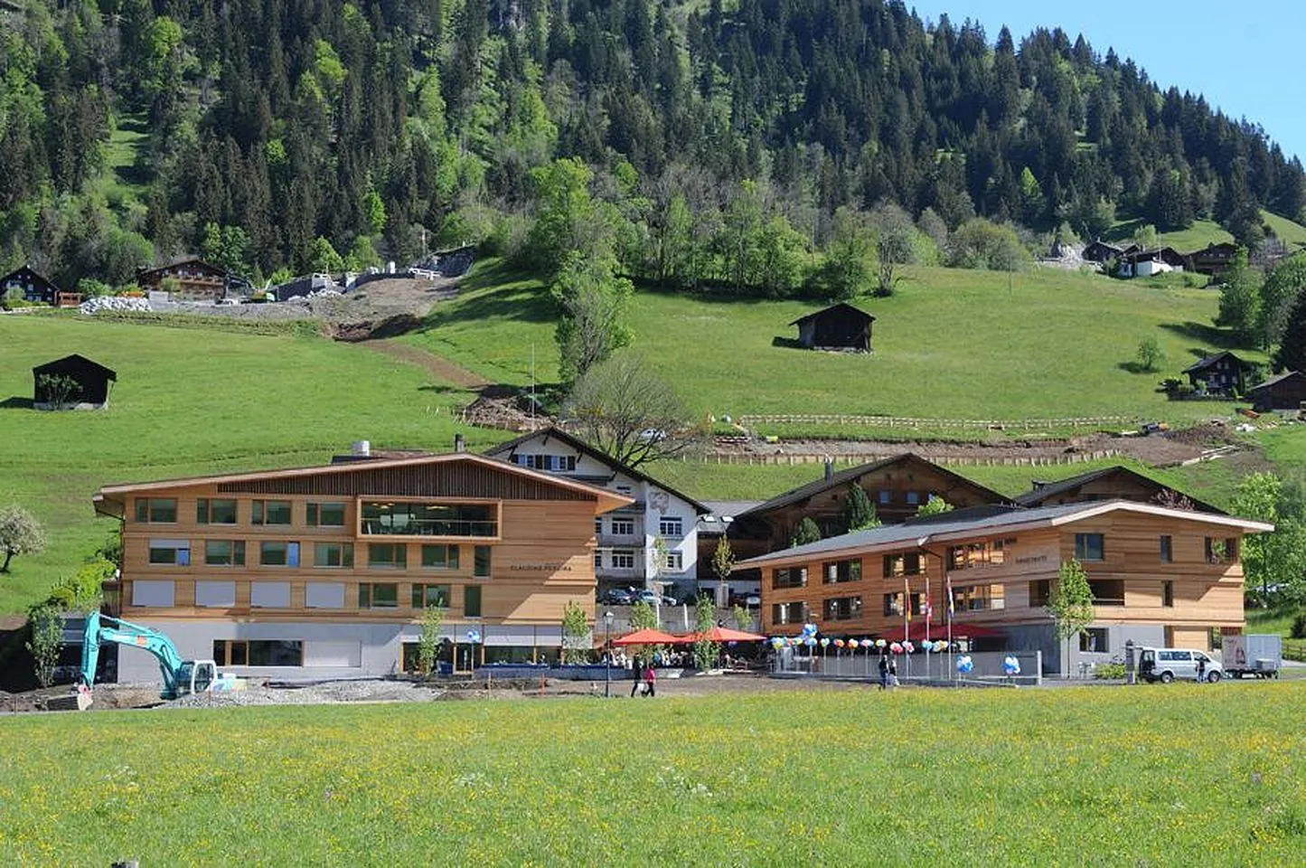 Alterszentrum Saanen, zwei Gebäude mit Holzfassade am Fuss eines bewaldeten Hangs