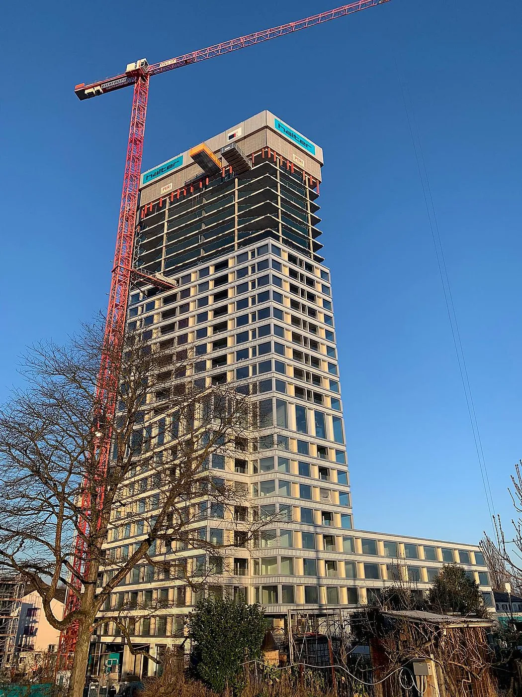 Bärentower Ostermundigen im Bau, Hochhaus mit rotem Baukran vor blauem Himmel