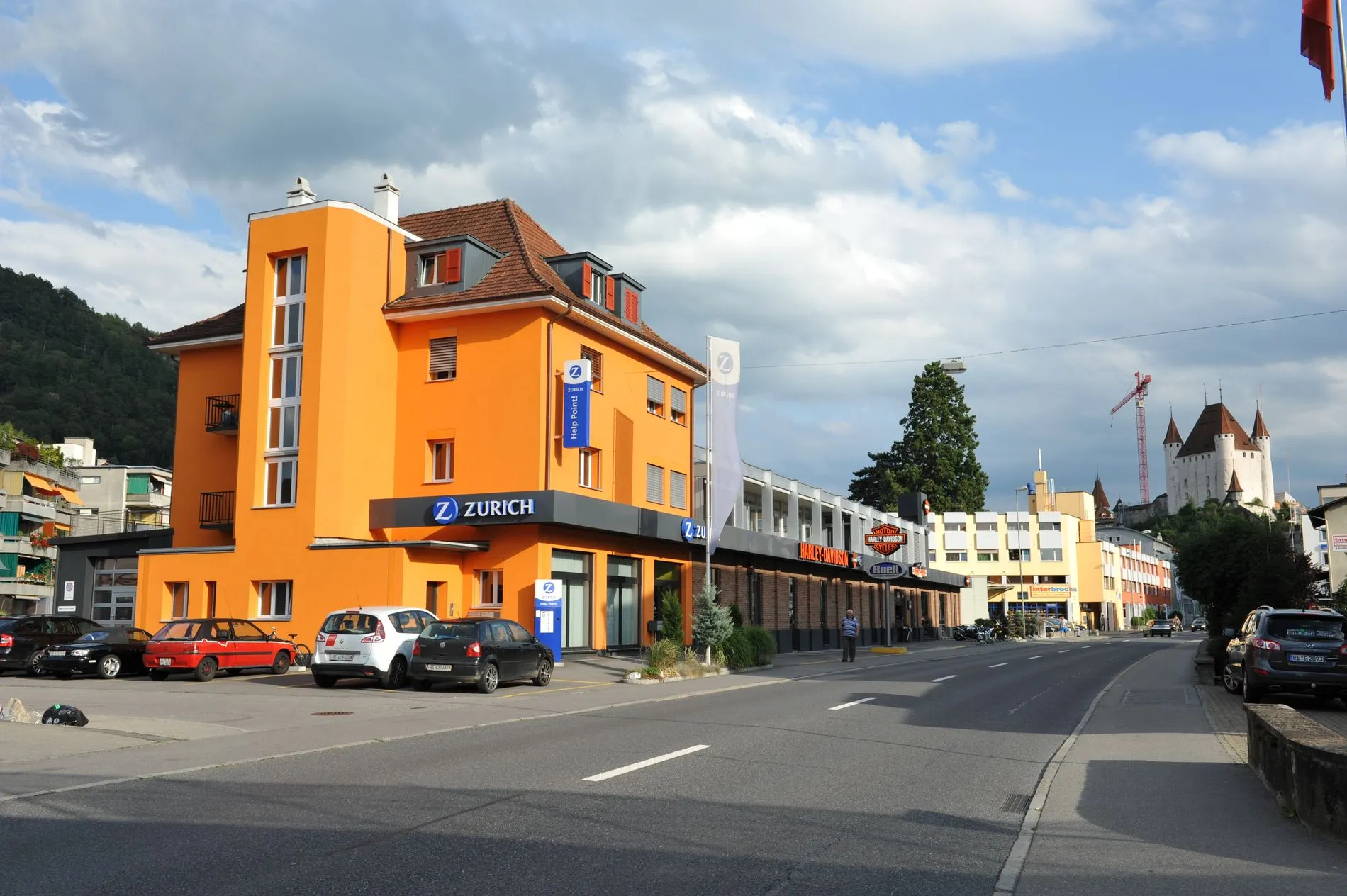 Orange gestrichenes Geschäftshaus an einer Strasse in Thun, im Hintergrund Schloss Thun