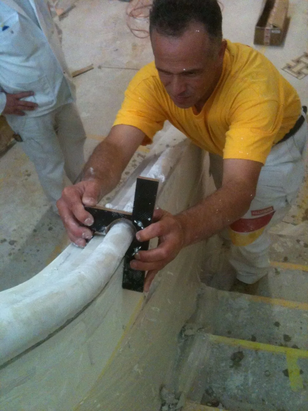 Ein Handwerker im gelben Shirt bearbeitet den Handlauf aus Stuck