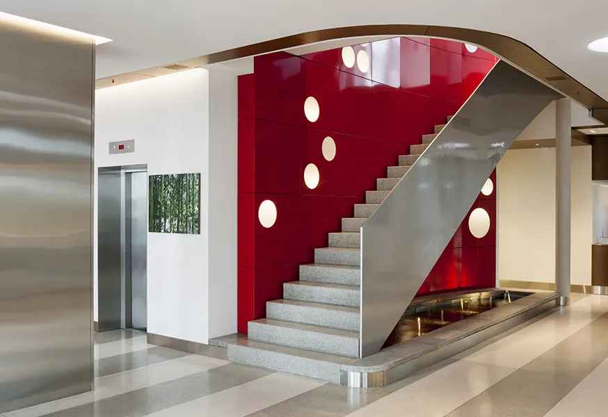 Treppenhaus im Hotel Ambassador Bern mit rot lackierter Wand, runden Leuchten und Edelstahlgeländer