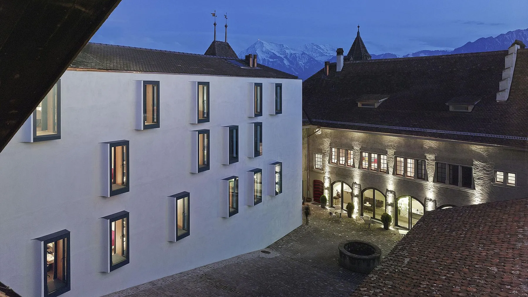 Schlosshof Thun in der Abenddämmerung, frisch verputzte weisse Fassade, im Hintergrund verschneite Berge
